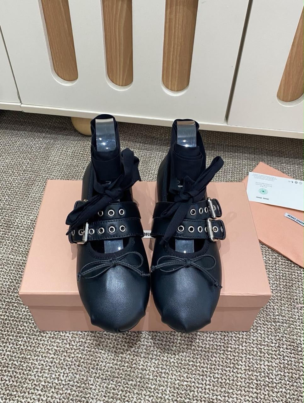 Miu Miu Buckled Leather Ballerina Shoes in black calf leather, featuring distinctive grommet-studded double buckle straps and delicate bow detailing