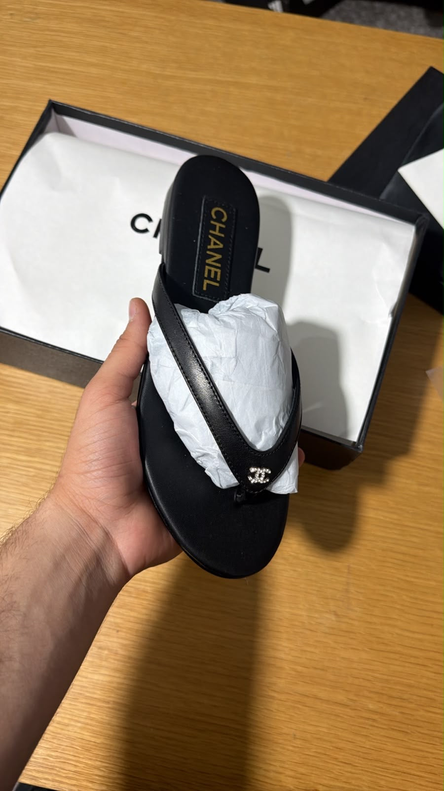 black leather Chanel thong flipflop accented with a signature crystal-embellished CC logo on the strap.