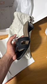 black Hermès Oasis sandals featuring the signature 'H' cut-out strap and a comfortable block heel.