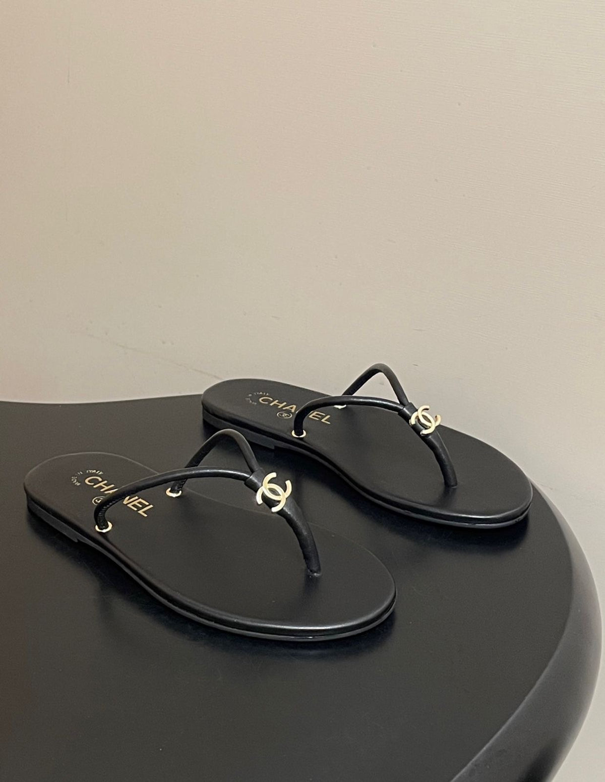 black leather Chanel thong flip-flop sandals featuring gold-tone interlocking CC logo hardware on the straps