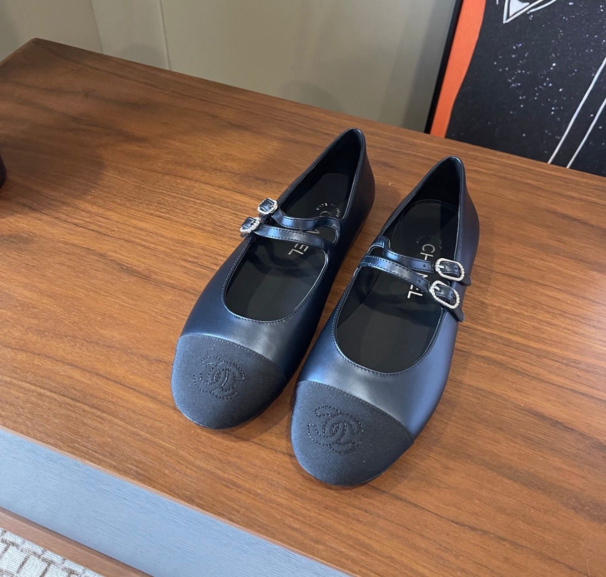 black Chanel Mary Jane flats featuring smooth leather bodies, double buckled straps, and grosgrain cap toes accented with an embroidered CC logo